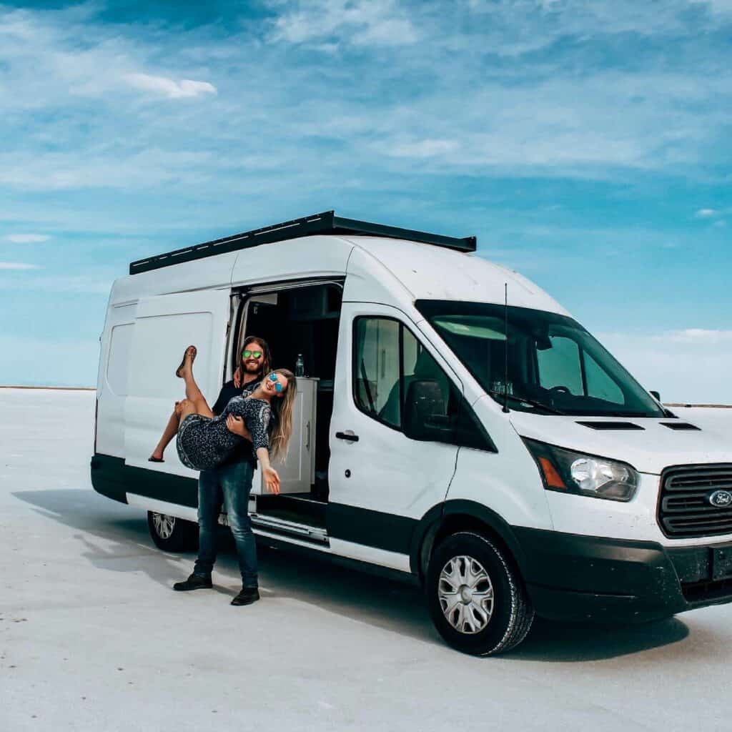 A couple poses outside of the Ford Transit van build that they live in