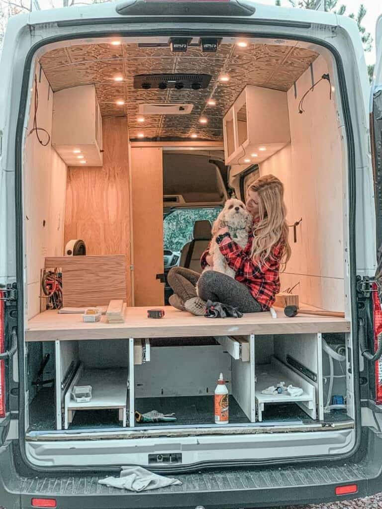 Woman with her dog poses inside her unfinished campervan build