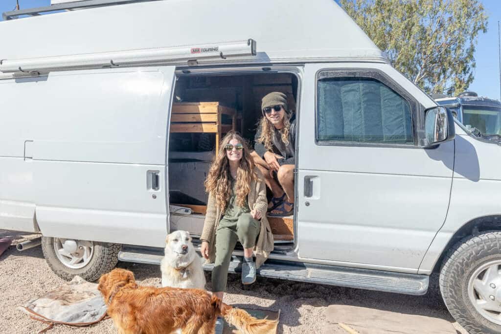 A man and woman pose with their dogs in the doorway of their campervan