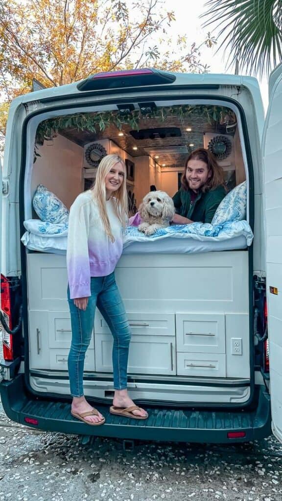 Couple and dog pose on their bed in their self-built campervan