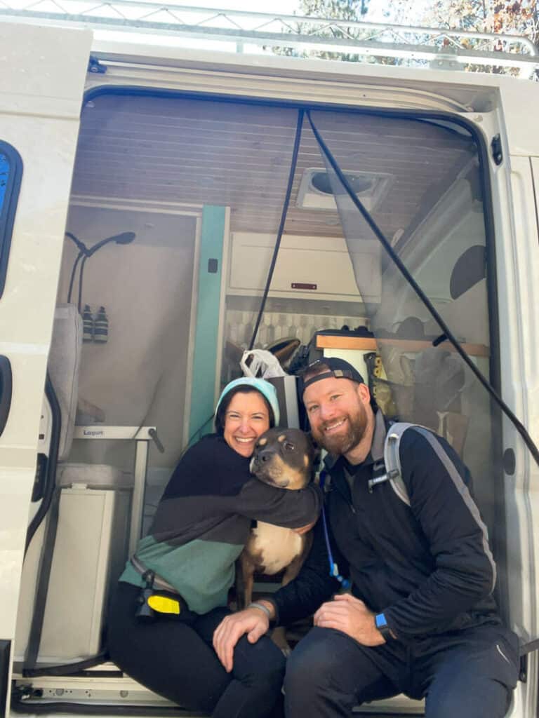 A Man and Woman posing with a dog in the doorway of a camper van