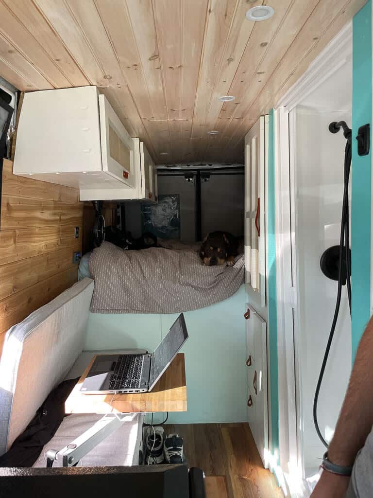 Couch with a desk and a large bed in the back in a camper van
