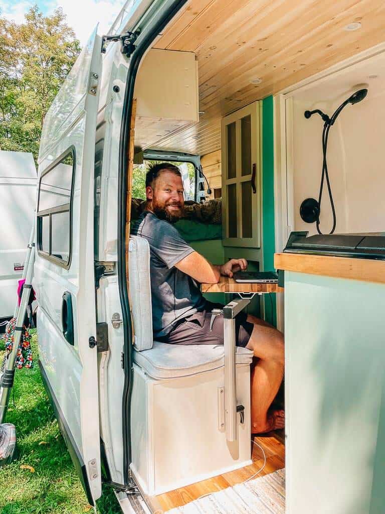 Man sitting on a couch and working on a laptop on a desk inside a campervan
