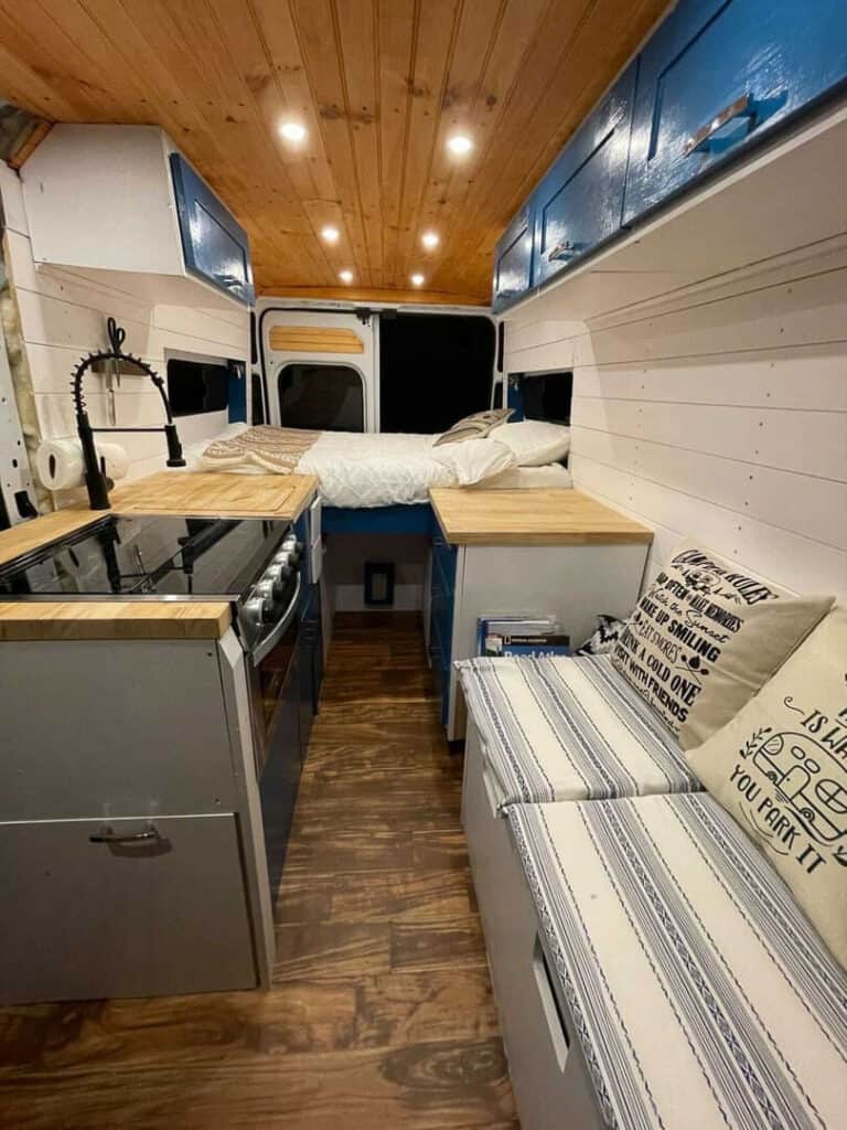 A campervan with full kitchen, bench seating and a bed with storage underneath