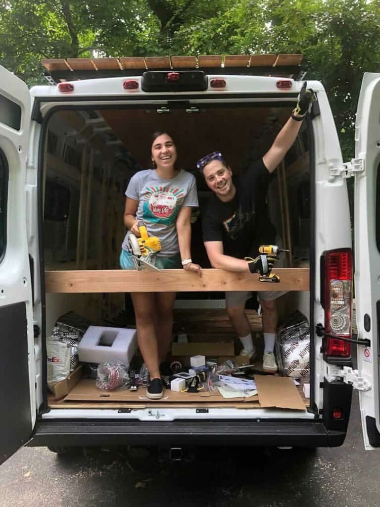 A woman and a man holding tools and standing inside the back of their van
