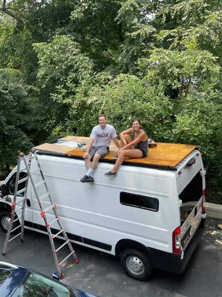 A man and a woman sitting on a wood roof deck on top of a van