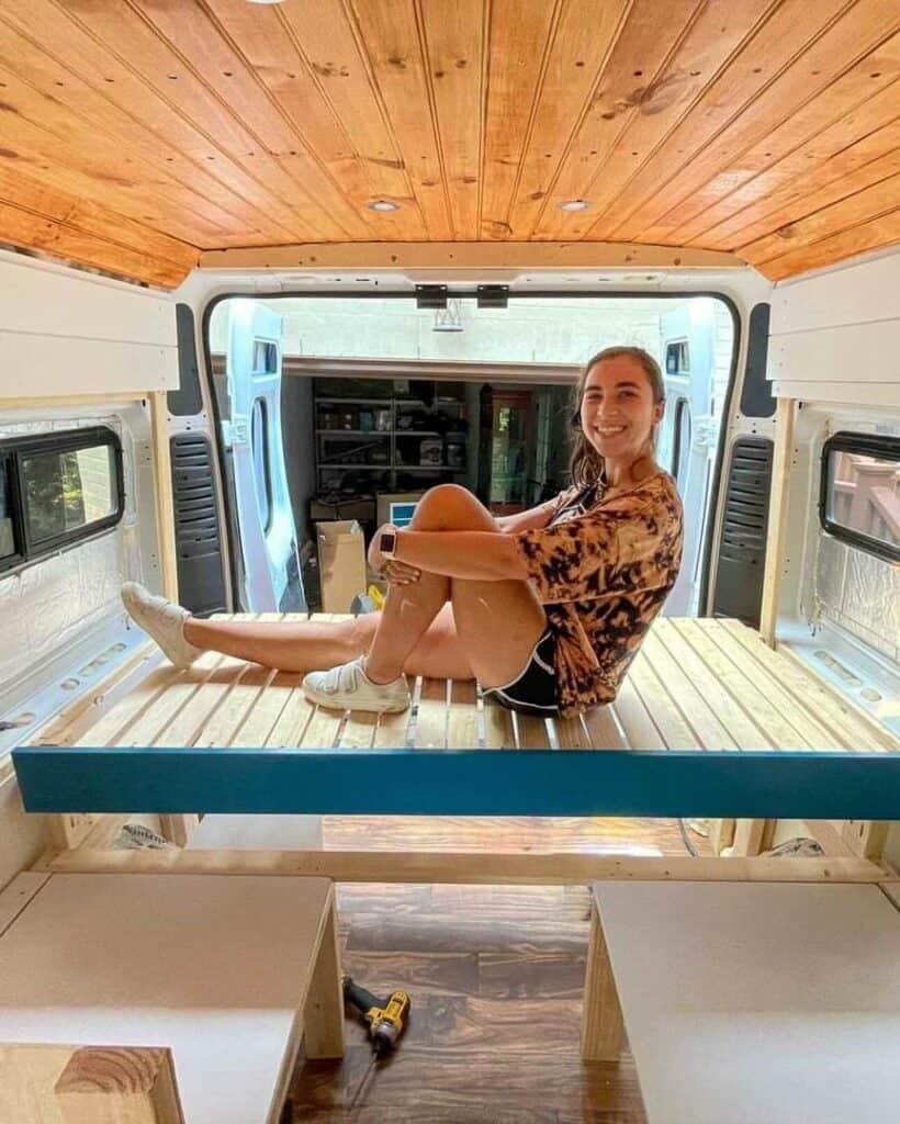 woman sitting on a bed frame in a unfinished campervan build