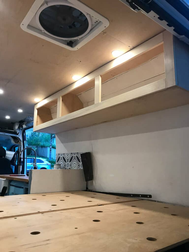 Bed platform in a camper van with unfinished cabinets above