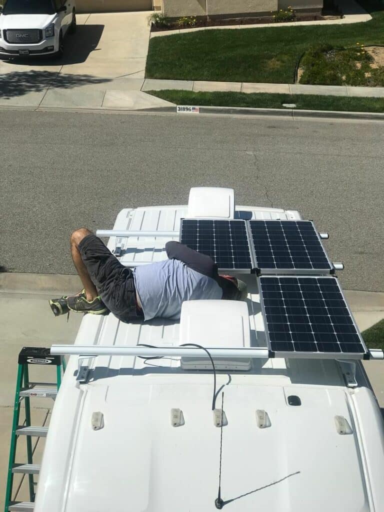 Man laying on the roof of a van installing solar panels