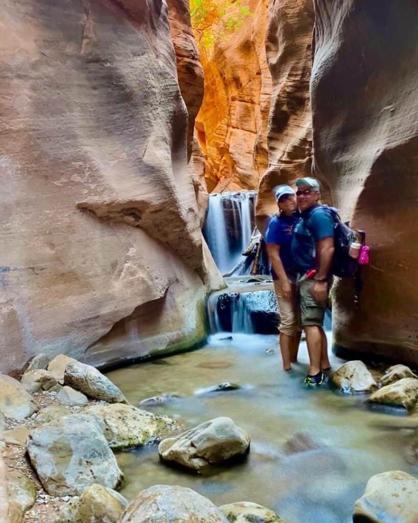 A man and woman posing in front of a small waterfall in a slot canyon