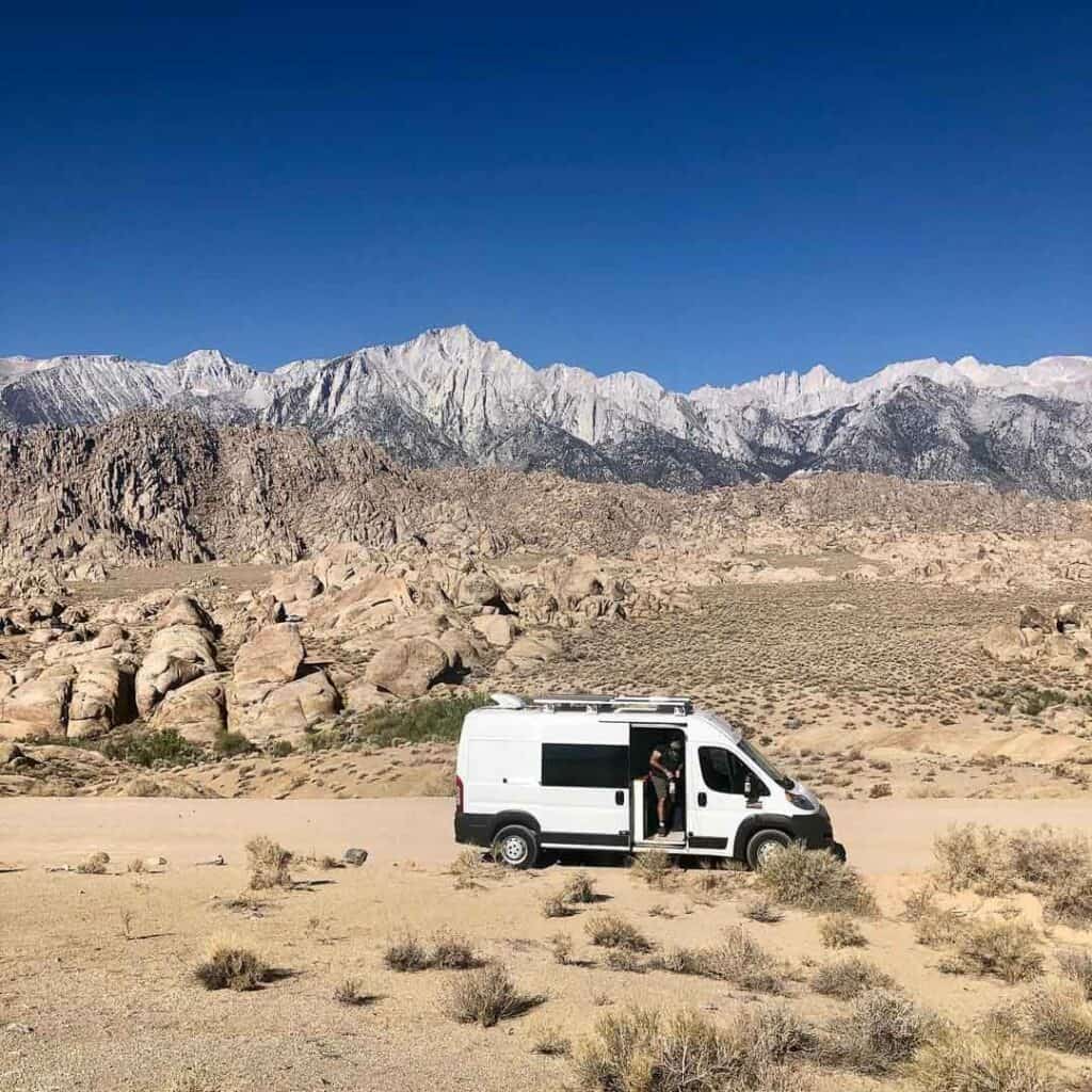 A van parked in the desert with a rocky mountain vista in the background