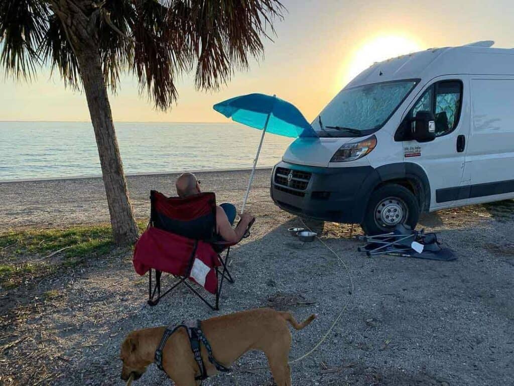 man sitting outside by campervan on beach