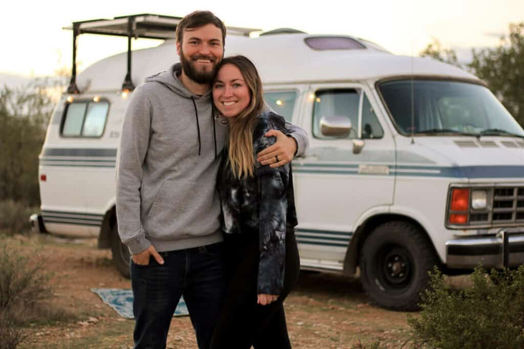 Man and Woman are all smiles as they stand outside of the campervan