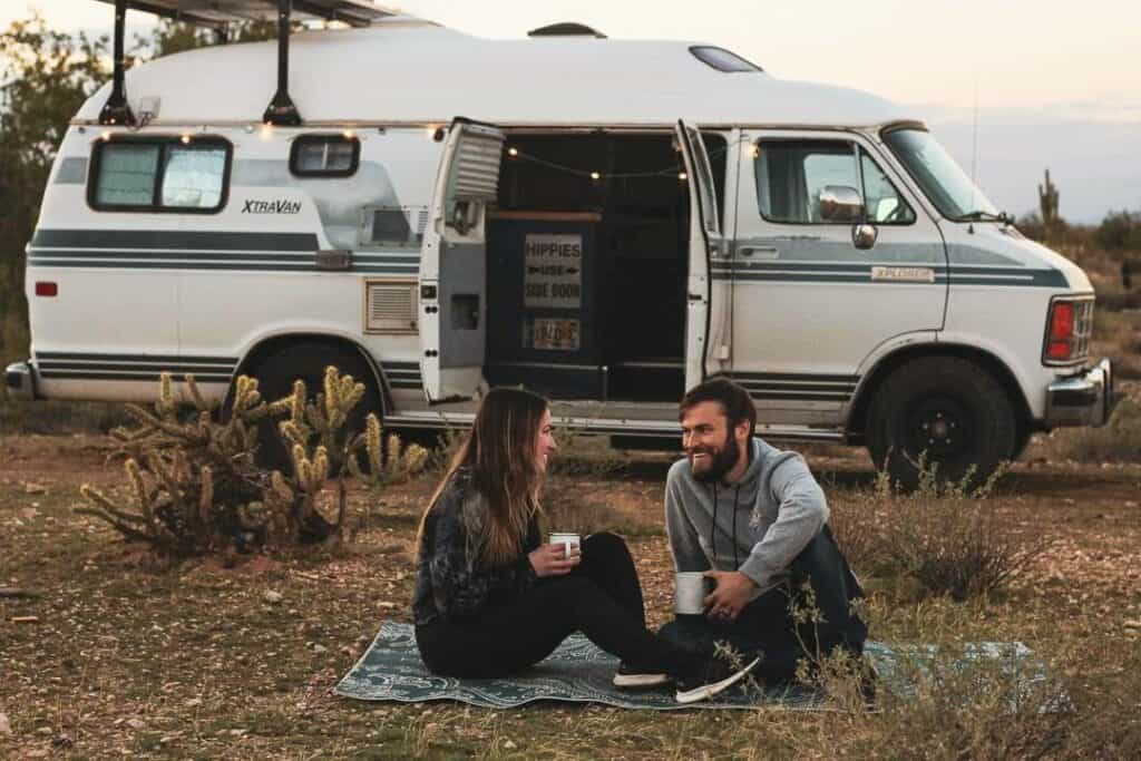 A man and a woman having a moment together while enjoying coffee as they sit outside of their camper van