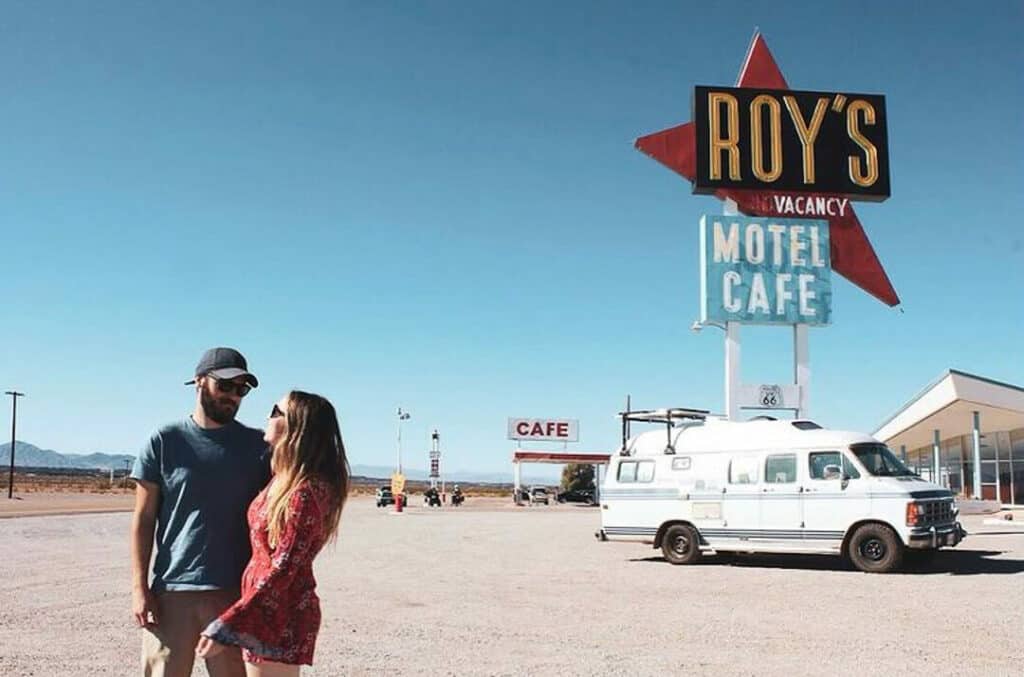 Man and woman standing outside of an old Motel with their camper van parked in the background