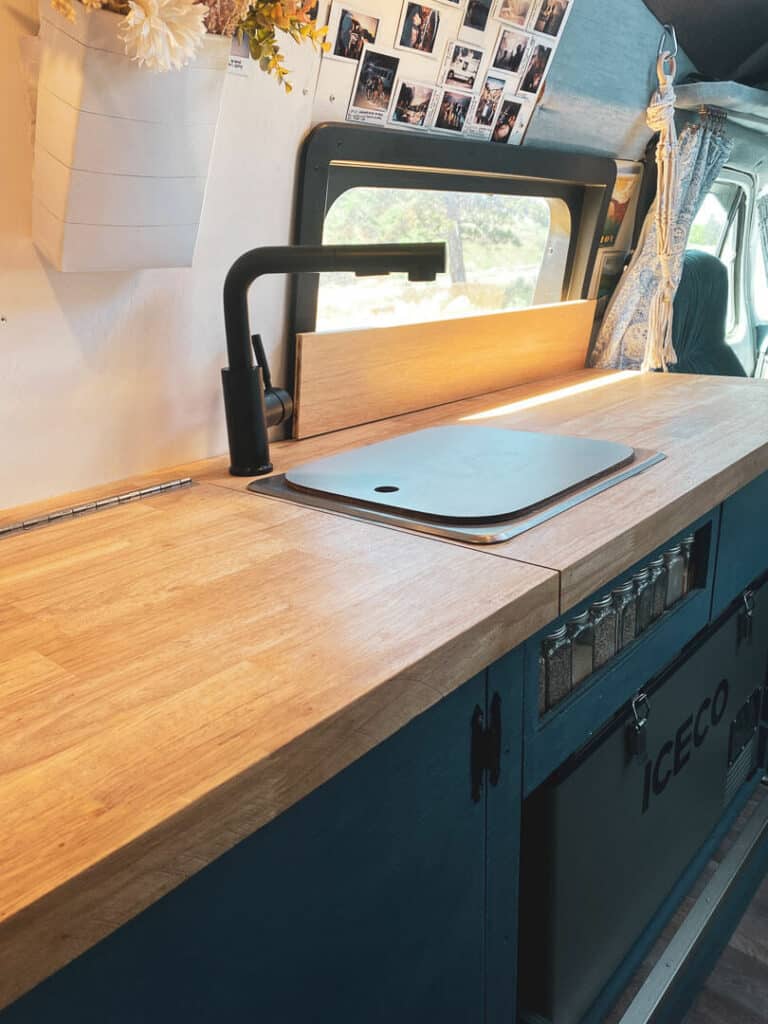 Butcher block counters with a small sink and faucet, a spice rack built into the cabinets and a Iceco chest fridge/freezer underneath in a campervan 