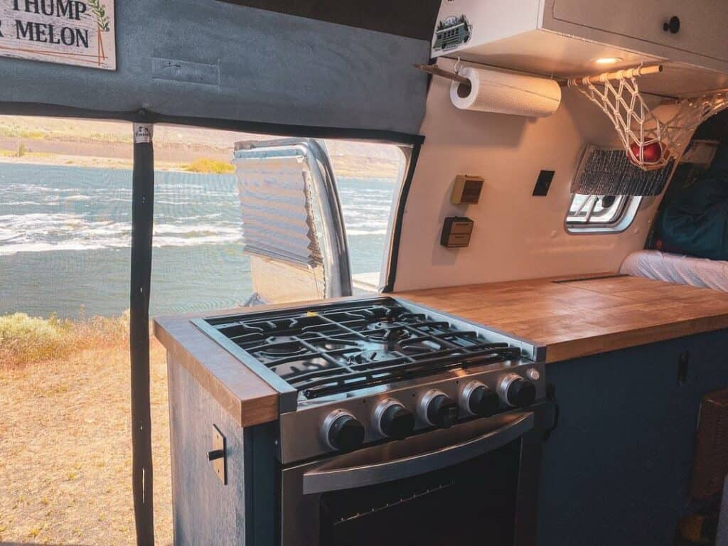 Butcher block counters and a stainless steel gas stove/oven combo in a camper van